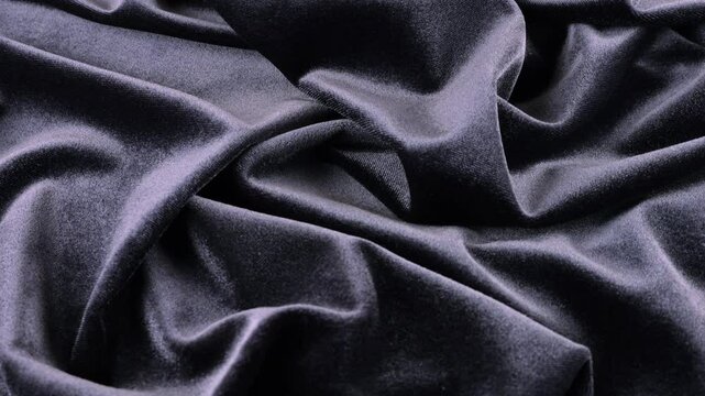 A luxurious velvet in a dark graphite color mauve shade. Textile background on theme design, fashion, tailoring and accessories. Beautiful folds of textured fabric on a rotating showcase. Top view.