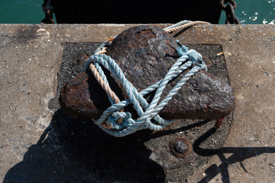 The steel marine mooring bollard embedded in concrete, used in maritime settings to secure vessels to the pier with ropes.