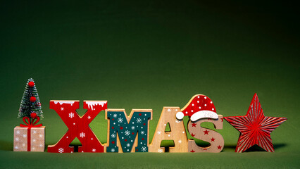 Xmas Schrift mit Weihnachtsm&uuml;tze, Weihnachtsbaum und Stern vor einem gr&uuml;nen Hintergrund