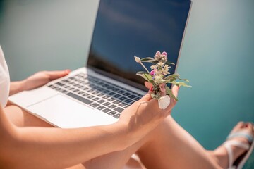 Freelance woman working on a laptop by the sea, typing away on the keyboard while enjoying the beautiful view, highlighting the idea of remote work.