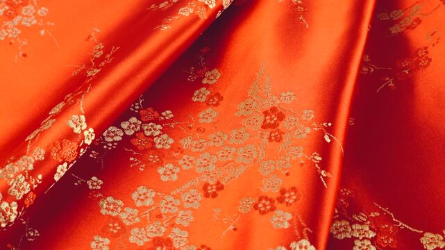 Lustrous red silk textile fabric background with floral golden embroidery in oriental style with plum blossom flower pattern. Soft folds of brocade shimmers beautifully on a rotating display case.