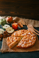 A cozy autumn setup featuring a freshly baked apple pie surrounded by apples, walnuts, a candle, and a warm drink
