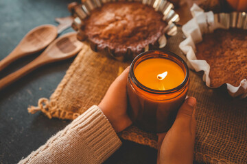 Burning candle in hands and pumpkin pie, cozy autumn