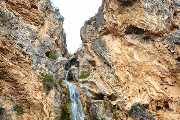 Rock Climber Ascending a Challenging Cliff Beside a Waterfall in a Natural Canyon During Daylight