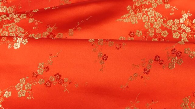 Lustrous red silk textile strawberry shade fabric background with floral golden embroidery in oriental style with plum blossom flower pattern. Soft folds of brocade shimmers.