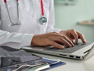 Closeup of doctor working on laptop computer with digital tablet on table in doctor's office...