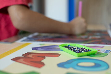 Fototapeta premium A child working on a colorful diamond painting of a lion, with alphabet learning materials and a pink stylus on a wooden desk.
