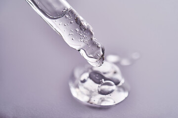 Pipette with facial serum pouring out of it on purple background.