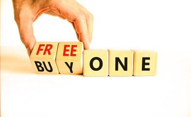 Buy and free one symbol. Businessman turns wooden cubes and changes words Buy one to Free one. Beautiful white table white background, copy space. Business Buy and free one concept.