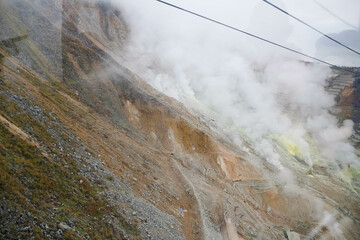 Owakudani, Japan- 29 Oct 2024: the volcano mountain with smoke and cable cars along the mountain with different colors rocks in yellow, brown and orange view from ropeway
