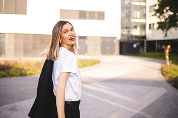 Beauty short hair woman holding jacket over shoulder. Successful happy woman on her way to work on street. Confident business woman walking with a smile. Happy female turn and walk with blazer.
