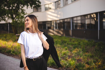 Beauty short hair woman holding jacket over shoulder. Successful happy woman on her way to work on street. Confident business woman walking with a smile. Happy female turn and walk with blazer.