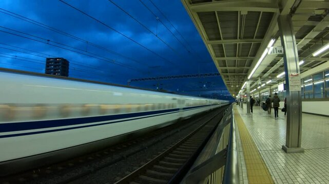 Japanese bullet train in blurred motion at nightfall, with passengers on the platform