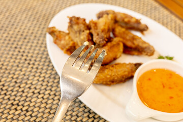 fried chicken wings on the plate served with dipping sauce so delicious and crispy. Defocused Thai style deep fried chicken wings  and a fork over the plate