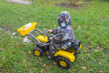 a child boy on a wheeled bulldozer tractor removes snow with a snow plow, photo without filters