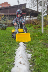 a child boy on a wheeled bulldozer tractor removes snow with a snow plow, photo without filters