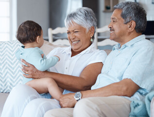 Fototapeta premium Love, laughing and grandparents with baby on sofa for bonding, smile and support. Relax, happiness and generations with senior man and woman holding child in living room of family home together