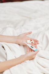 Person holding thermometer and pills in bed, another person with thermometer healthcare concept
