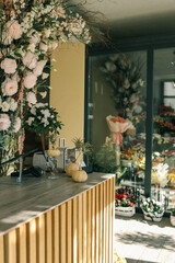 Flower shop interior with a wooden counter decorated with small pumpkins, vases, and plants. The background shows floral arrangements, bouquets