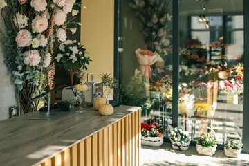 Flower shop interior with a wooden counter decorated with small pumpkins, vases, and plants. The background shows floral arrangements, bouquets