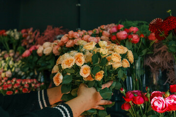 Close-up of hands arranging a bouquet of fresh roses in a flower shop. Vibrant roses in shades of...