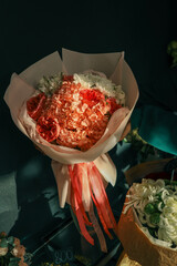 A vibrant bouquet of pink and peach flowers wrapped in pastel paper with a satin ribbon, displayed in dramatic light against a dark background, exuding elegance and charm