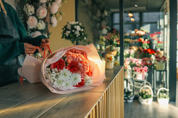 Close-up of a luxurious bouquet featuring vibrant red roses, delicate hydrangeas, and white alstroemerias, elegantly arranged and wrapped in soft pastel paper on a wooden counter