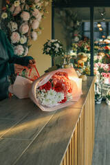 Florist arranging a bouquet of pink and pastel flowers on a wooden counter with a blurry flower shop in the background. Captures the essence of floral arrangement and natural beauty