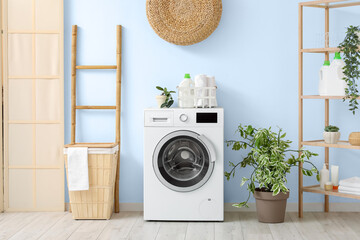 Modern washing machine with basket, shelving unit and ladder near white wall. Interior of home...