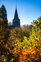 Slate-covered church spire of “Kloster Oelinghausen“ standing out from the autumnal colorful trees. Historic Premonstratensian convent or nunnery in Sauerland in the middle of a wonderful scenery.