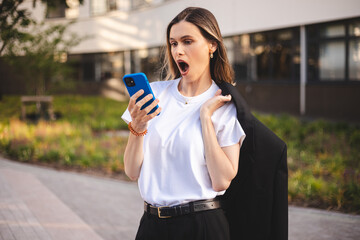 Beauty short hair woman holding jacket over shoulder. Business woman stupor with something occurring in social media, wow omg emotions. Woman hold mobile phone and look shock because of news.