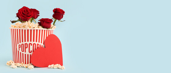 Bucket of popcorn with beautiful red roses and paper heart on blue background. Valentine's Day celebration © Pixel-Shot