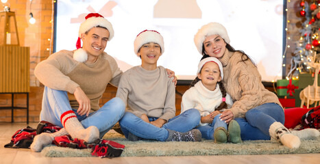 Happy family in Santa hats watching Christmas movie on projector screen at home
