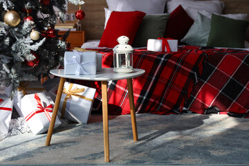 Glowing lantern with Christmas gift boxes on table in festive bedroom