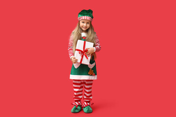 Cute little girl in Christmas elf costume holding gift box on red background
