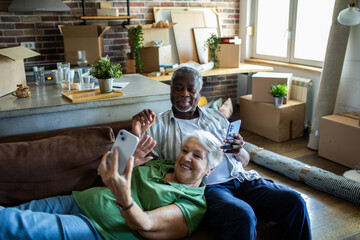 Senior couple relaxing on couch with smartphones after moving in