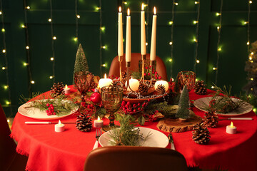 Festive dining table set for Christmas with burning candles and fir cones in room