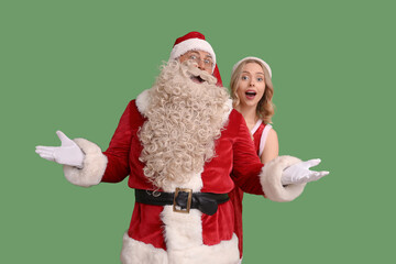Surprised Santa Claus and beautiful young woman on green background