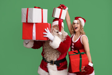 Funny Santa Claus and beautiful young woman with Christmas gifts on green background