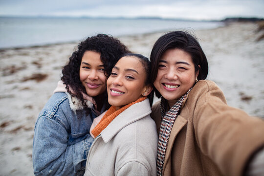 Three young women friends taking a selfie on a windy beach