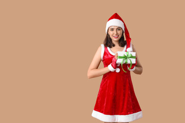 Young woman in Santa Claus costume with Christmas gift box on brown background
