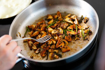 There is frying pan with pieces of champignons and green asparagus shoots on gas stove. Home cooking of delicious dishes according to recipes of cookbook © JackF