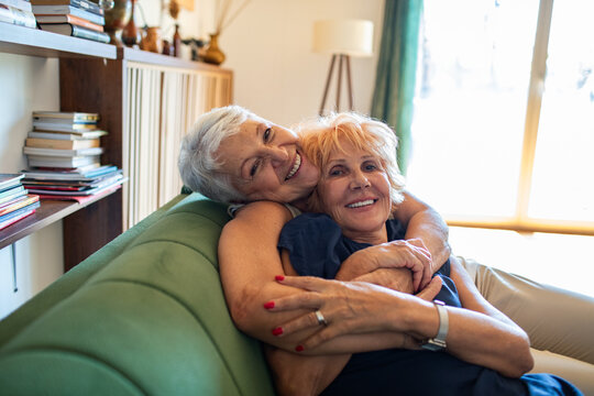 Portrait of a smiling senior lesbian couple embracing on couch at home - Powered by Adobe