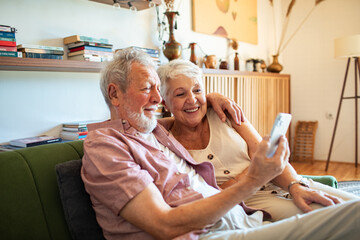 Obraz premium Happy senior couple video calling family on smartphone at home