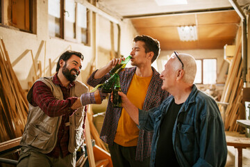 Small group of carpenters enjoying a cold bottle of beer after a hard days work in their woodworking workshop