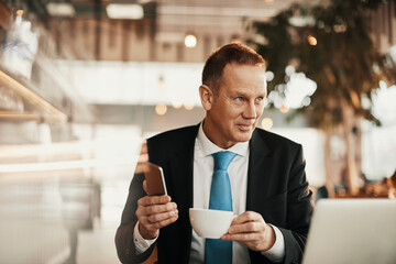 Middle aged businessman having coffee while using his laptop in a cafe bar decorated for christmas and the new year holidays