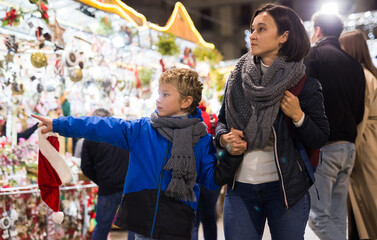 Fototapeta premium Portrait of smiling cute preteen boy walking with his mother at colorful Christmas street market. Happy family moments