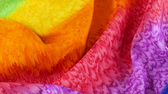 Soft folds of fabric hand-dyed in bright rainbow colors. Color gradients and textile texture close-up on a rotating display case. Textile background on the theme is LGBTQ community.