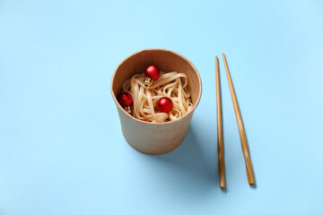 Takeaway box with chinese noodles, Christmas balls and chopsticks on color background