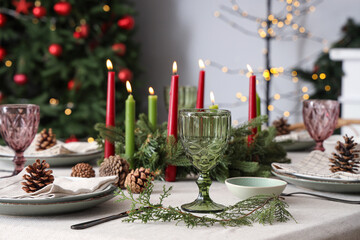 Festive table setting with Christmas decorations, burning candles and pine cones in dining room, closeup